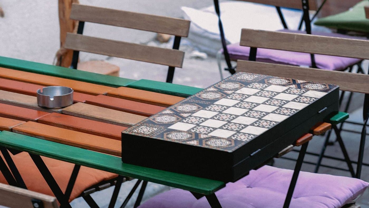 An inlaid checkered board set up on an outdoor cafe table.