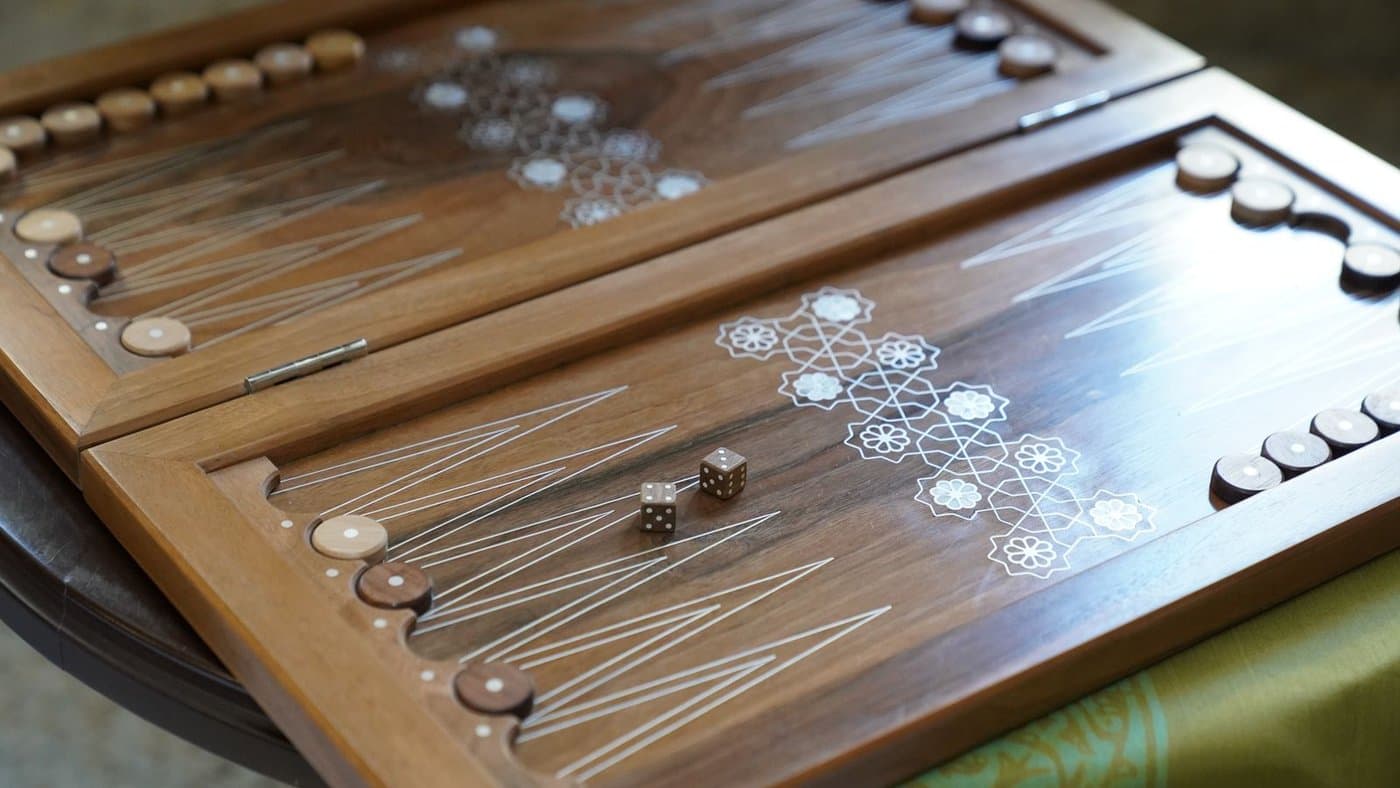 A wooden backgammon board with mother-of-pearl inlay, set up and ready to play.