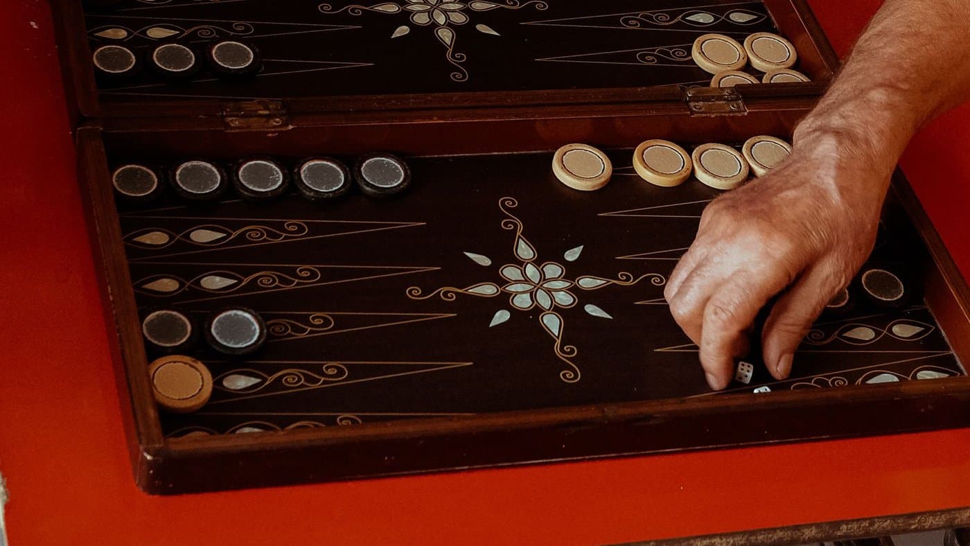 A hand arranging checkers and dice on an ornate backgammon board.